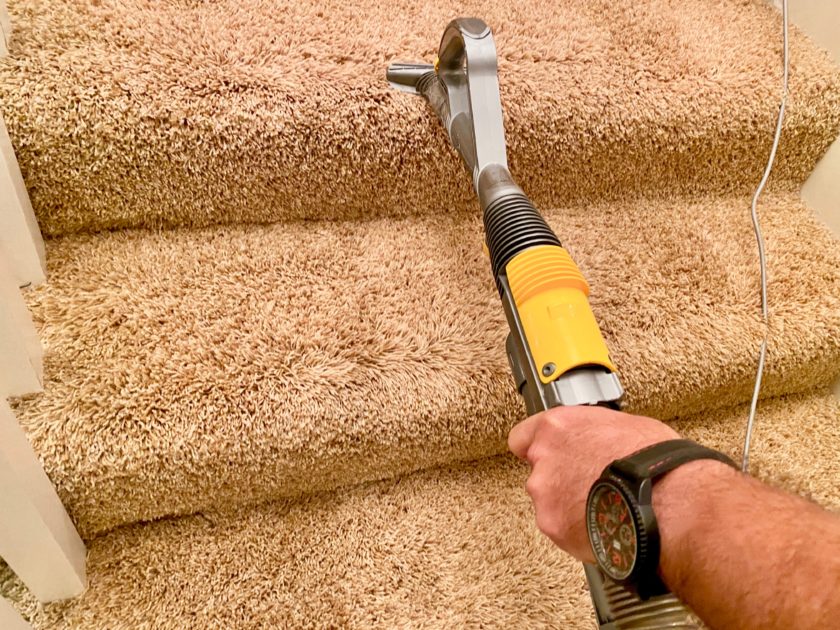 Vacuuming carpeted stairs with a handheld vacuum.