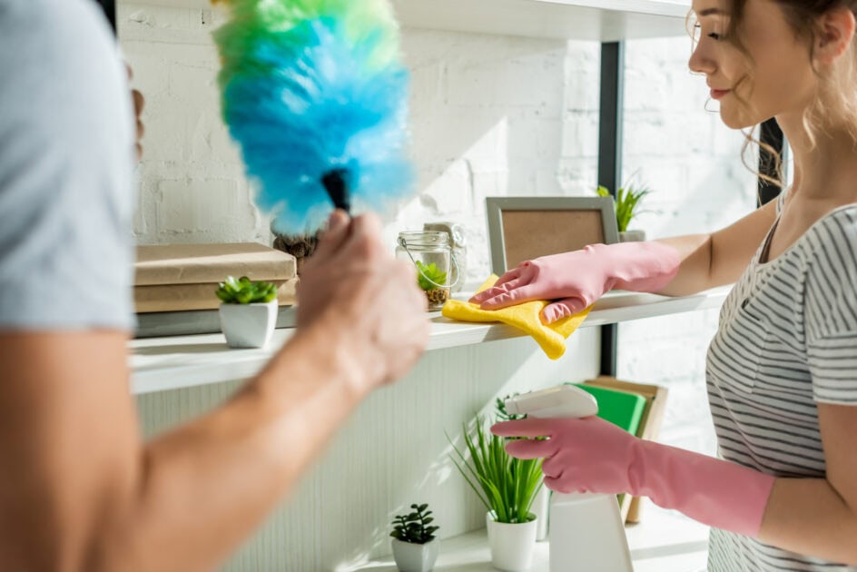 Two people cleaning shelves with duster and cloth, using the 20-minute cleaning rule for efficiency