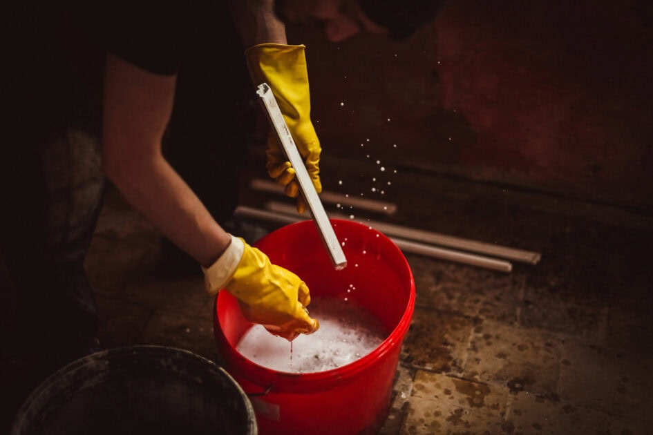 Man wearing yellow gloves cleaning construction dust from a red bucket with soapy water