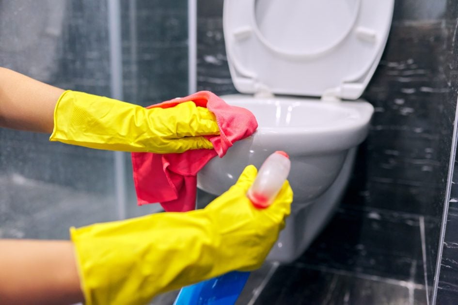 A person disinfects a toilet bowl using cleaning solution and a red cloth.